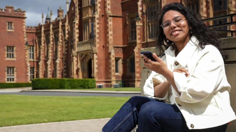 student sitting looking at phone in front of Queen